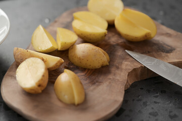 Raw washed and chopped baby potatoes ready to cook on olive wood board