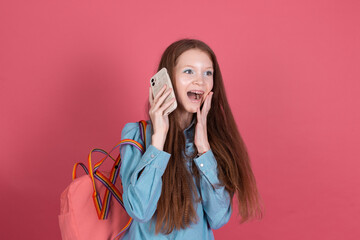 Little kid girl 13 years old isolated on pink background schoolgirl with backpack with mobile phone...