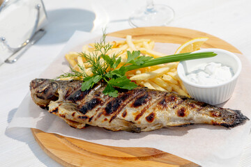 grilled fish garnished with herbs and fries