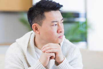Fototapeta na wymiar young asian man sitting on sofa at home pensive, worried about problems and depression. male has an experience relationships at work or family, problems with loan repayment debt Seriously conceived