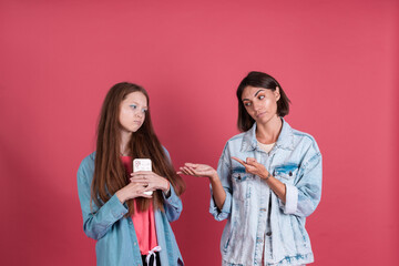 Modern mom and daughter in denim jackets on terracotta background, girl  with phone and mom stands by trying to take phone