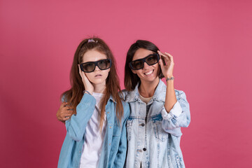 Modern mom and daughter in denim jackets on terracotta background in 3 d cinema glasses watching comedy movie together, smiling