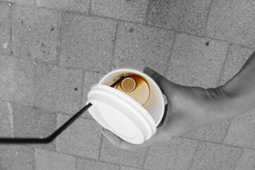 A two euro coin at the bottom of a paper coffee cup. Leftover coffee and a plastic tube. Hold a glass in your hand against a background of paving stones.