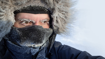 Traveler in the Arctic. Portrait of a freezing man in winter clothes, a hood and a warm mask. Ice...