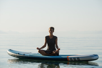 Young woman meditating in peace on a sup board