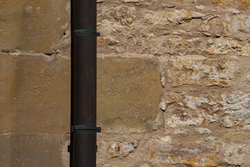 Fototapeta na wymiar Downpipe in front of a sandstone and natural stone wall with copy space