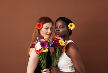 Two women of different races with flowers in their hairs holding bouquets. Caucasian and African...