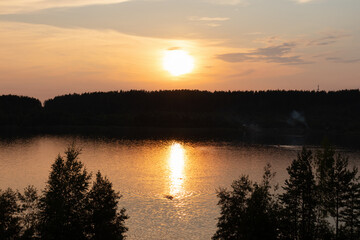 Obraz premium Lake or river in the light of sunset among trees, reflection of sun in the water