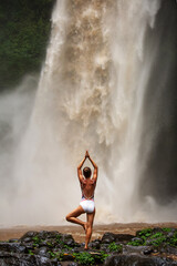 Beautiful woman doing yoga near a waterfall in Bali