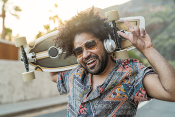 Happy Afro skater having fun listening to music with headphones during summer time - Youth people...