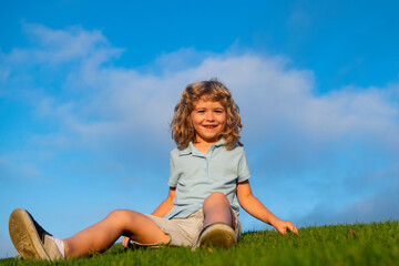 Fototapeta premium Happy child boy sitting on green grass outdoors in spring park.