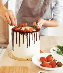 Young female makes biscuit cake with chocolate and strawberries in the kitchen.