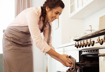 A young woman bakes muffins, takes them out of the oven, puts the pastries in the oven.