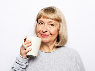 Cheerful elderly woman wear casual with cute smile holding a cup of coffee over white background. Lifestyle and people concept.