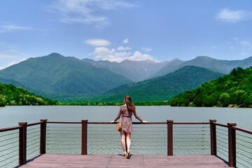 Traveler girl standing alone on edge of pier and staring at lake and mountains. Enjoying beautiful freedom moment life and serene quiet peaceful atmosphere in nature. Back view