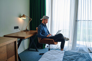 Millennial casual caucasian man freelancer sit at chair in hotel room and remote working online...