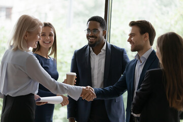 Happy confident senior businesswoman, business leader, coach getting acquainted with new team of employees, interns, students, standing and shaking hands with worker at informal meeting