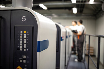 Close up view of modern offset printing machine and operators in working uniform checking quality...