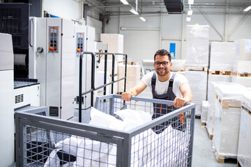 Worker moving cart full of wasted paper in printing house.
