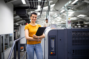 Portrait of talented female designer standing by modern printing machine in print shop.