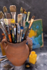 Paint brush in clay jug and palette on table background. Paintbrush for painting as art still life