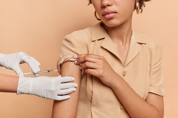Unknown person with dark skin makes covid 19 vaccination gets injection dose in shoulder wears brown dress in one tone with background. Coronavirus treatment inoculation and prevention concept