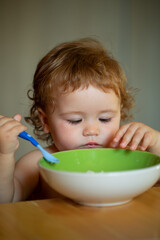 Kid baby eat soup in the kitchen with dishes and spoon. Child nutrition concept.