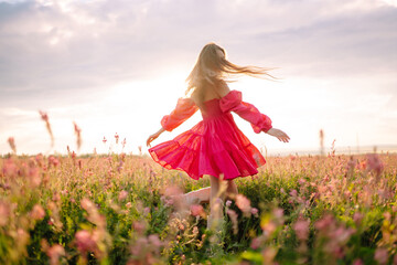 Stylish woman in a pink dress posing in the blooming field. Nature, vacation, relax and lifestyle....