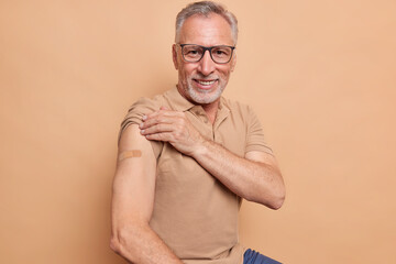 Senior man in spectacles shows plastered arm after getting coronavirus vaccine happy to feel safe...