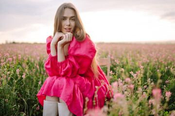 Stylish woman in a pink dress posing in the blooming field. Nature, vacation, relax and lifestyle....