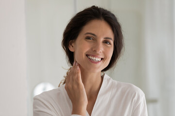 Young hispanic female with perfect healthy white smile pose for portrait in bathroom touch neck...