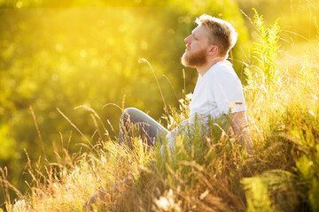 Bearded young man sitting on the grass on a summer day