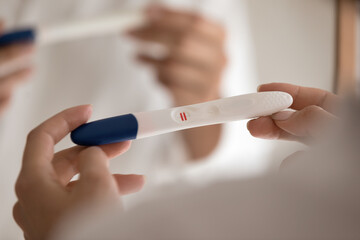 Two bars. Cropped close up view of millennial pregnant female hands holding domestic compact test showing positive result on screen. Young lady detecting pregnancy after ivf using home stick test kit