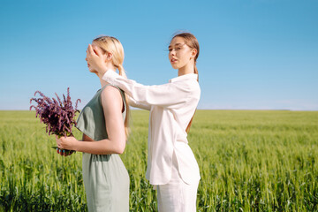 Portrait of two fair-haired girls in fashionable and stylish clothes, against the background of a field. Nature, vacation, relax and lifestyle. Fashion concept.