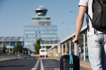 Passenger walking from bus station to airport terminal. Selective focus on hand holding suitcace.