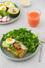 Healthy delicious breakfast, sandwich with avocado and salmon, cucumbers and radishes and microgreens of peas with boiled egg and corn salad, grapefruit smoothie in a glass