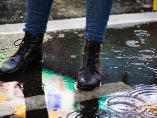 Feet with black boots on standing in a puddle and colorful  neon lights reflection 