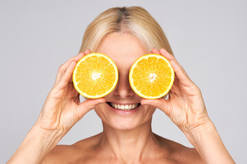 Mature woman closes her eyes with a sliced orange.