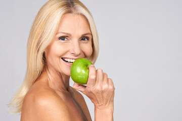 Cheerful smiling mature woman is biting a green apple.