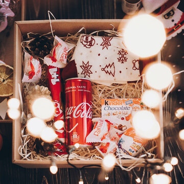 Lviv, Ukraine - December 1, 2017: Coca cola can, stylish socks, kitkat,  kinder chocolate on straw in gift box with christmas lights. Top view. Gift box for christmas, birthday, fathers day