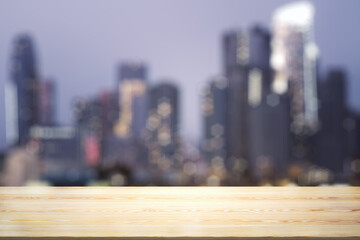 Empty wooden table top with beautiful blurry skyscrapers at evening on background, mock up