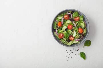 Cucumbers and tomatoes, red onion and spinach mix in fresh vegetables salad in grey bowl plate on white background.