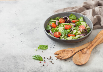 Spatula fork and spoon with bowl of healthy vegetarian vegetables salad with tomatoes and cucumber, lettuce and spinach on light background.