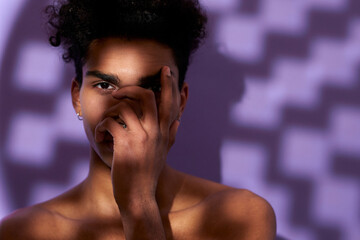 Close up portrait of fit male model posing in shadow on purple background. Transgender young man
