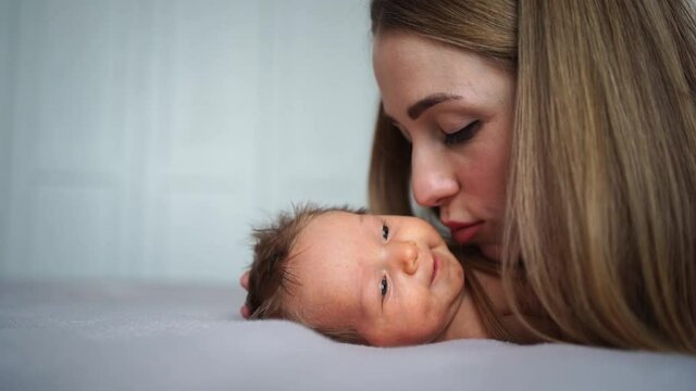mom gently kisses the baby on the bed. maternal love and care. care for newborns
