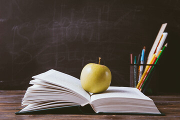  book, apple, pens, chalk,  markers on a black blackboard background