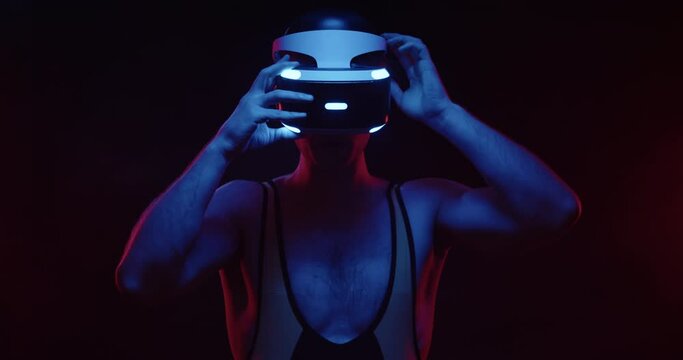 Future handsome man in tracksuit puts on VR glasses helmet and prepares to dive into virtual reality on black background. Cyberpunk men play virtual reality online game using modern 3D VR headset