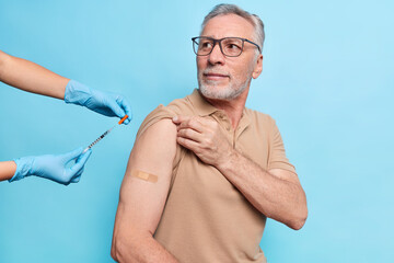 Senior man with grey beard engaged in free vaccination program gets vaccine in arm listens...