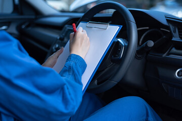 Close-up of an unrecognizable mechanic wearing blue jumpsuit uniform, sitting inside the car,...