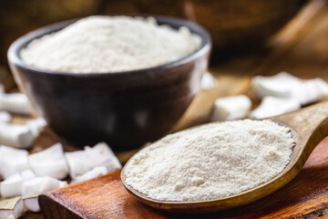 full rustic wooden spoon and coconut flour, on wooden table with coconut in the background, culinary ingredient.